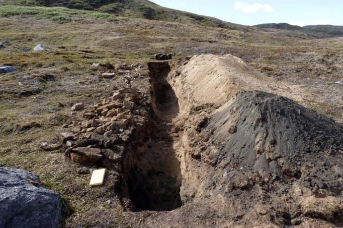 A 2010 trench cut across a rare-earth-bearing carbonatite dyke on a grassy hillside, with spoil heaped beside it